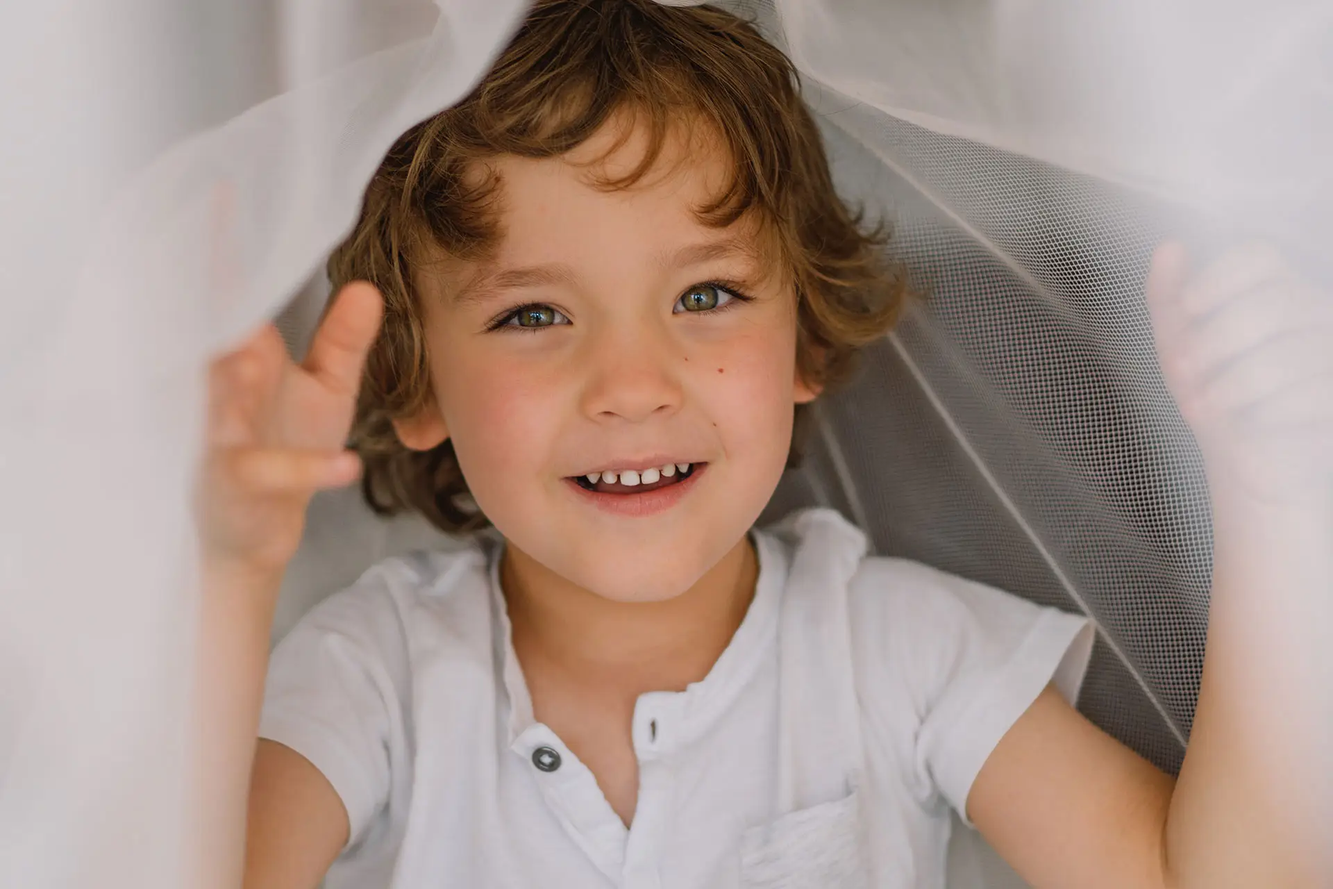 A close up of a happy child coming out from under a fine white netting